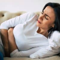 Dysmenorrhea. Close-up photo of a woman, who is lying on her sofa and holding her stomach with suffering facial expression.